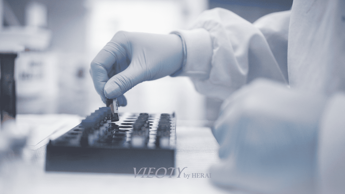 光が差す研究室で、白衣を着たVIEOTY開発者が処方箋を手に真剣な表情で考え込んでいる様子。背景には医薬部外品のラベルと化粧品のラベルが並んでいる。